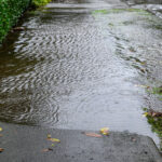 Heavy rain caused flooding over sidewalk, grass strip, and road.